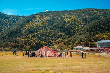 A wide, panoramic landscape showing the immense scale of the Yila Grassland and Napahai Lake, with people scattered across the plain.