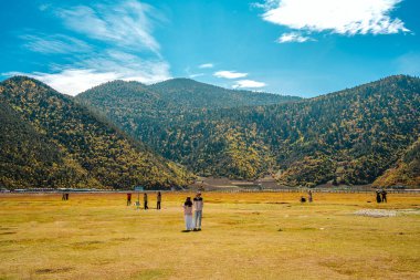 A wide, panoramic landscape showing the immense scale of the Yila Grassland and Napahai Lake, with people scattered across the plain.