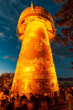 Shangri-La, Çin - 21 Ekim 2024: Seyyahlar ve turistler Dafo Tapınağı 'ndaki dev, parıldayan dua çarkını döndürerek ruhani enerjiyi bulanıklaştırıyor..