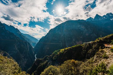 Tahta patika uçurumun kenarındaki dramatik vadiye tutunur. Balagezong, Shangri-La 'da. Dağlık tepeler ve mavi gökyüzü üzerinde güneş doğar..