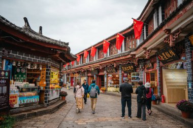 Lijiang, Çin - 23 Ekim 2024: Ziyaretçiler, Çin 'in Lijiang Eski Kasabası' ndaki ahşap dükkanlar ve tarihi çatılarla kaplı taş geçidi, bulutlu gökyüzünün altında keşfediyorlar..