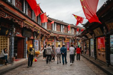 Lijiang, Çin - 23 Ekim 2024: Ziyaretçiler, Çin 'in Lijiang Eski Kasabası' ndaki ahşap dükkanlar ve tarihi çatılarla kaplı taş geçidi, bulutlu gökyüzünün altında keşfediyorlar..