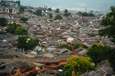 Lijiang Eski Kasabası 'nın geleneksel kiremitli çatılarına bakan arka planda dağlar ve bulutlu gökyüzü.