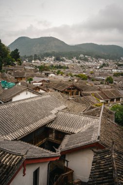 Lijiang Eski Kasabası 'nın geleneksel kiremitli çatılarına bakan arka planda dağlar ve bulutlu gökyüzü.