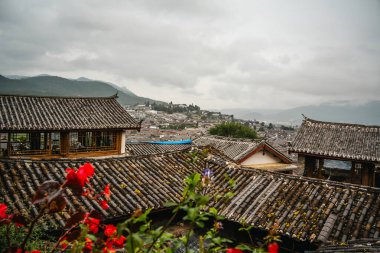 Lijiang Eski Kasabası 'nın geleneksel kiremitli çatılarına bakan arka planda dağlar ve bulutlu gökyüzü.