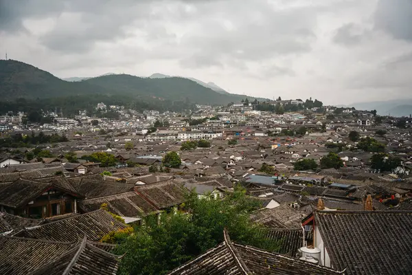Lijiang Eski Kasabası 'nın geleneksel kiremitli çatılarına bakan arka planda dağlar ve bulutlu gökyüzü.