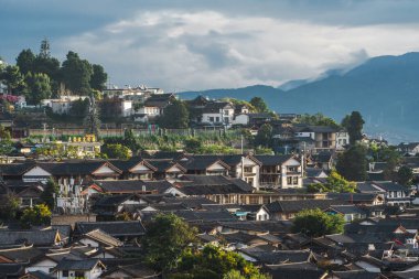 Lijiang Eski Kasabası 'nın engin geleneksel çatı manzarası ufukta dağlarla birlikte dramatik bulutlu bir gökyüzünün altında uzanır..