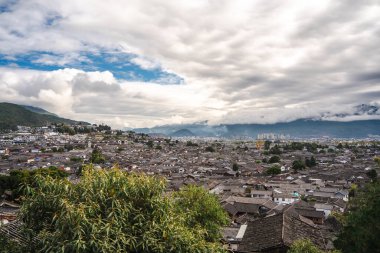 Lijiang Eski Kasabası 'nın engin geleneksel çatı manzarası ufukta dağlarla birlikte dramatik bulutlu bir gökyüzünün altında uzanır..