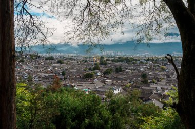 Lijiang Eski Kasabası 'nın engin geleneksel çatı manzarası ufukta dağlarla birlikte dramatik bulutlu bir gökyüzünün altında uzanır..