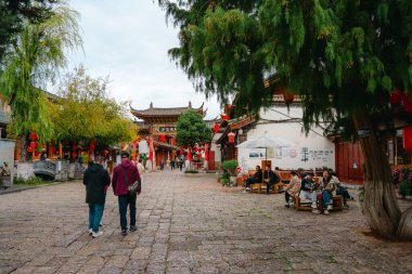 Lijiang, Çin - 25 Ekim 2024: Lijiang Old Town, Yunnan 'da turistler, Çin bayrakları ve tarihi sokağı süsleyen geleneksel kırmızı fenerlerle dolu canlı sokak sahnesi.
