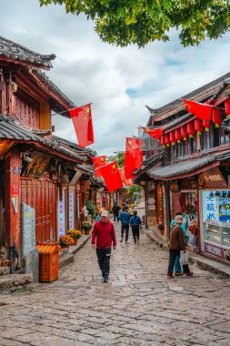Lijiang, Çin - 25 Ekim 2024: Lijiang Old Town, Yunnan 'da turistler, Çin bayrakları ve tarihi sokağı süsleyen geleneksel kırmızı fenerlerle dolu canlı sokak sahnesi.