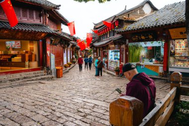 Lijiang, Çin - 25 Ekim 2024: Lijiang Old Town, Yunnan 'da turistler, Çin bayrakları ve tarihi sokağı süsleyen geleneksel kırmızı fenerlerle dolu canlı sokak sahnesi.