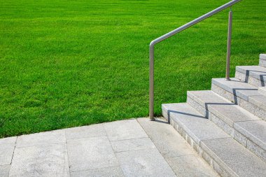 Güneşli bir yaz gününde yeşil bir çimenlik boyunca taş merdivenleri ve çelik parmaklıkları olan granit kaldırım, yürümek için peyzaj yapılmış bir park, hiç kimse. 
