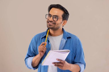 Genç adam başka tarafa bakıyor ve elinde kalem ve defterle düşünüyor.