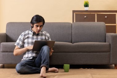 Genç çocuk oturma odasında yerde otururken dizüstü bilgisayar kullanıyor.