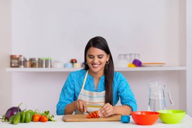 Indian woman chopping tomato with knife in kitchen clipart