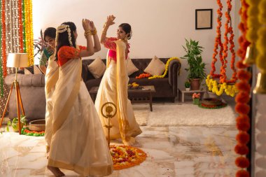 Onam vesilesiyle beyaz sari giymiş kadınlar birlikte dans ediyorlar.