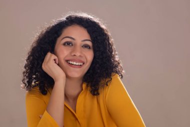 Elleri yanağında güzel genç bir kadın gülümseyerek yukarı bakıyor.