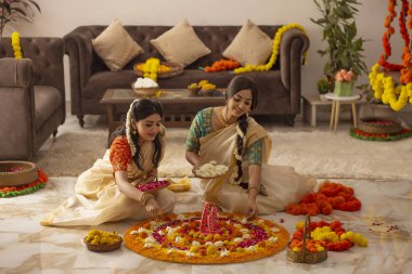 Beyaz sarili Güney Hintli kadınlar Onam 'ı kutlamak için çiçeklerle dekore ediyorlar.