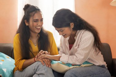 İki genç kadın oturma odasında kanepede otururken bir ışık anı paylaşıyorlar.