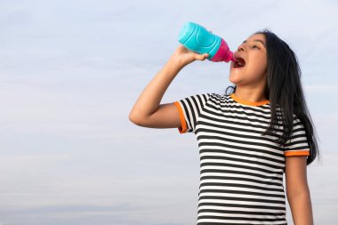 Mavi gökyüzüne karşı dururken susamış kız su şişesi içiyor.