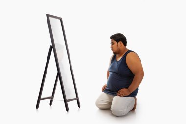 Portrait of a fat man looking at bellyfat mirror in despair against plain background. clipart