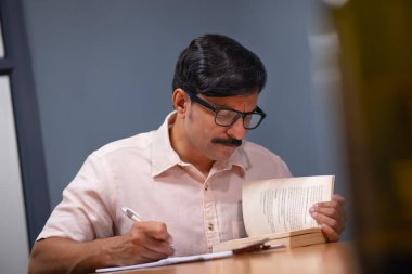 Adult man reading book and taking notes at home clipart