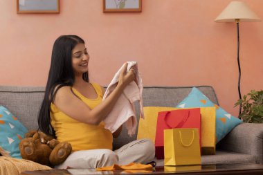 Hamile kadın, daha doğmamış bebeği için ilk kıyafetleri izliyor.