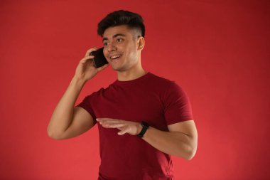 Genç adam kırmızı arka planda cep telefonuyla konuşuyor.