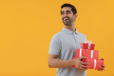 Happy young man holding gifts in his hands against yellow background clipart