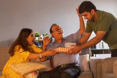 Abisi, babasıyla kanepede otururken kız kardeşine hediye veriyor.