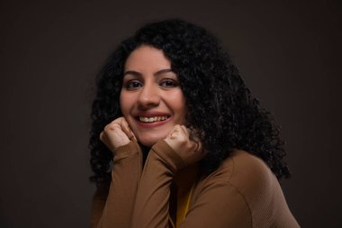 İki eli çenesinde, gülümseyen genç bir kadın.