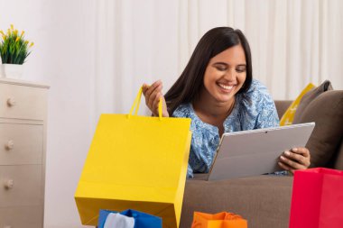 Kanepeye uzanmış elinde alışveriş torbasıyla tablet izleyen Hintli kız.