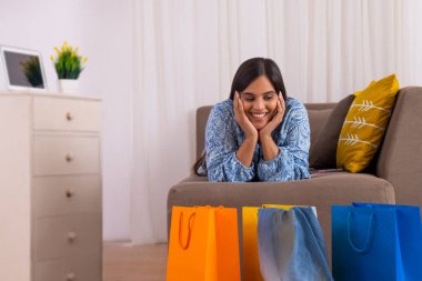 Hintli kız alışveriş yaptıktan sonra mutlu bir şekilde kanepede uzanıyor.