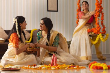 İki kadın Onam 'da yerleri çiçeklerle süslerken diğer kadınlar salıncakta oturuyor.