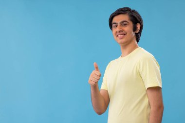 Mavi arka planda dikilen gülümseyen gencin portresi