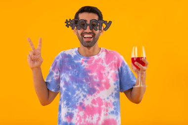 Parti gözlüklü, şarap kadehi tutan ve parmaklarıyla el kol hareketi yapan komik genç adam.