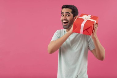Mutlu genç adam pembe arka planda hediyesini tutuyor.