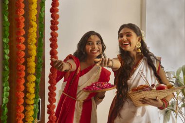 Durga Puja vesilesiyle evde puja thali ile duran geleneksel kıyafetli iki Bengalli kız kardeşin portresi.