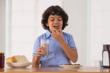 Elinde bir bardak milkshake tutarken kurabiye yiyen bir çocuğun portresi