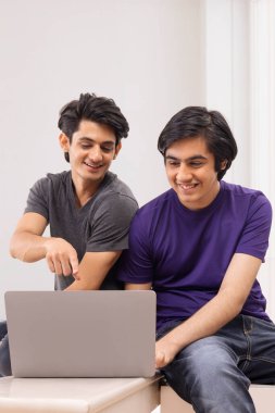 Düz arkaplanda dizüstü bilgisayar kullanan iki gencin portresi