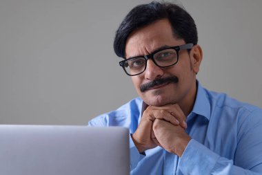 Orta yaşlı bir adam ofis işi yaparken kameraya bakıp gülümsüyor.