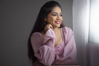 Pencerenin yanında oturan genç bir kadın ve elleri yanaklarında dışarı bakıyor.