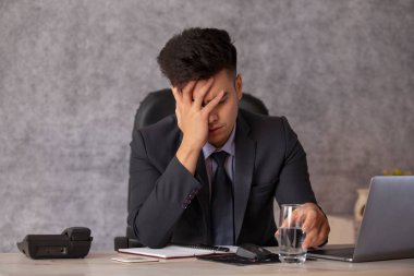 Ofiste eli başında oturan stresli genç bir iş adamının portresi.