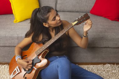 Oturma odasında gitar çalan genç bir kadın.