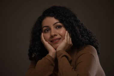 Elleri yanağında bir kadının yakın plan portresi. Başka tarafa bakıyor ve düşünüyor.