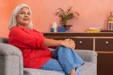 Oturma odasında kanepede dinlenen yaşlı bir kadının portresi.