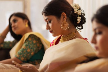 Geleneksel kıyafetli kadınlar arkadaşlarıyla birlikte kanepede otururken cep telefonu kullanıyorlar.