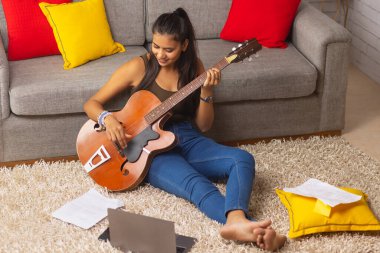 Genç kadın evde oturma odasında gitar çalmak