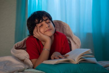 Çocuk yatakta kitap okurken düşünüyor.